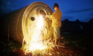 Chatarrero desguazando los restos de un cohete mientras anochece. Foto: Jonas Bendiksen